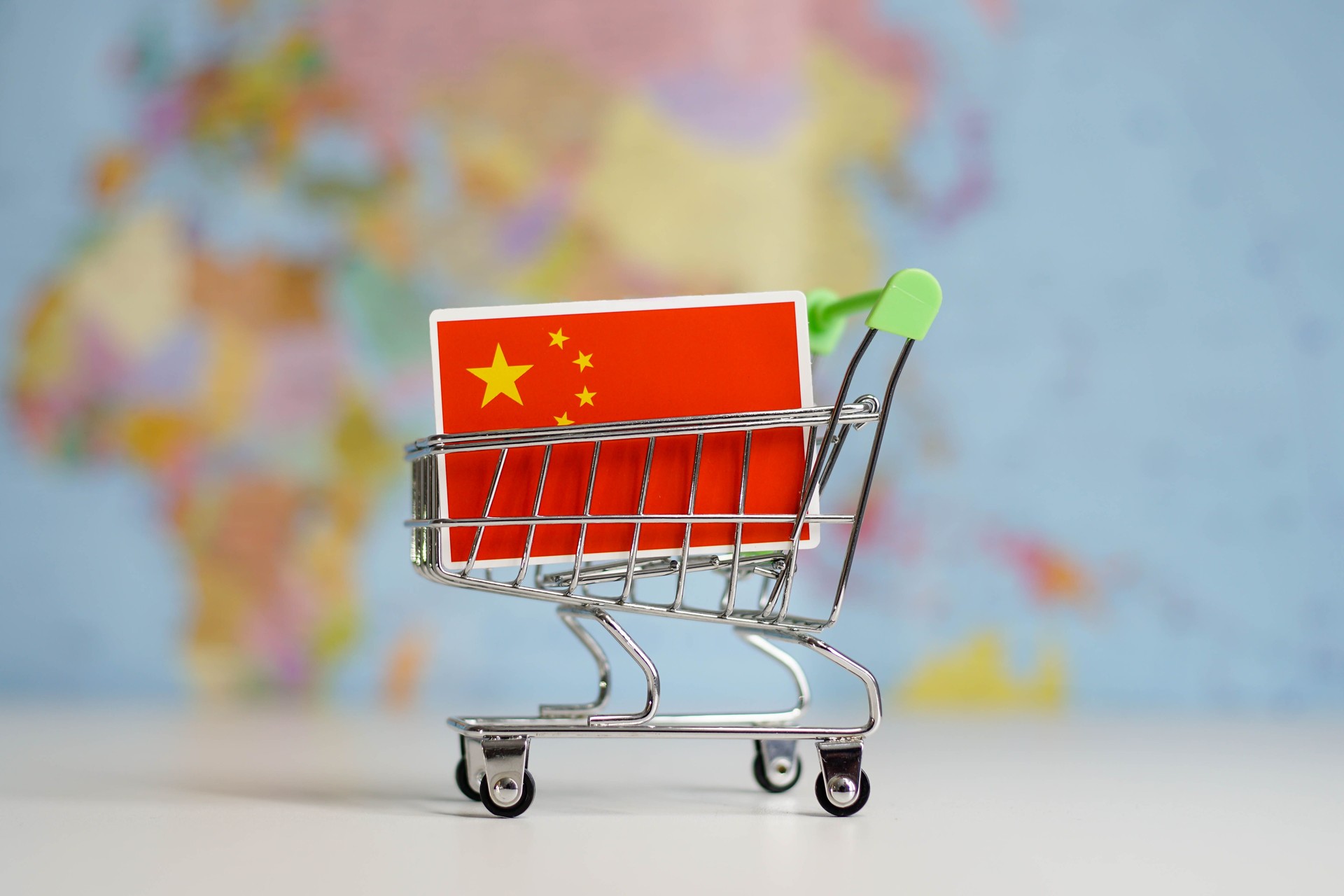 China national flag in miniature shopping trolley cart. Shopping online or shipping, duty concept. World map on the background.